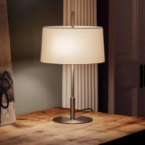 Diana Mayor table lamp illuminated on wooden tabletop showing warm ambient lighting and minimalist brushed silver finish in home interior setting