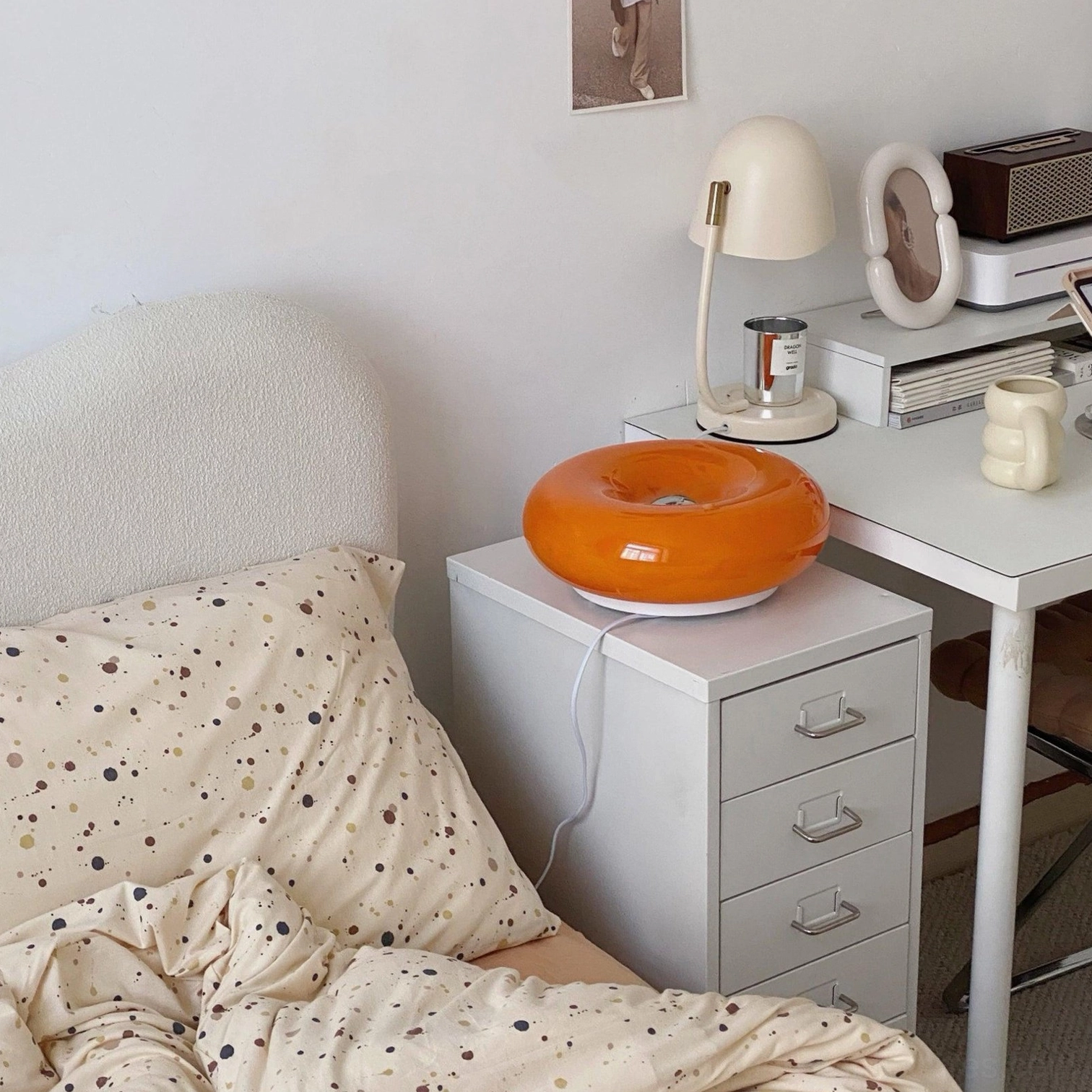 Orange donut table lamp on white bedside cabinet in modern neutral bedroom interior