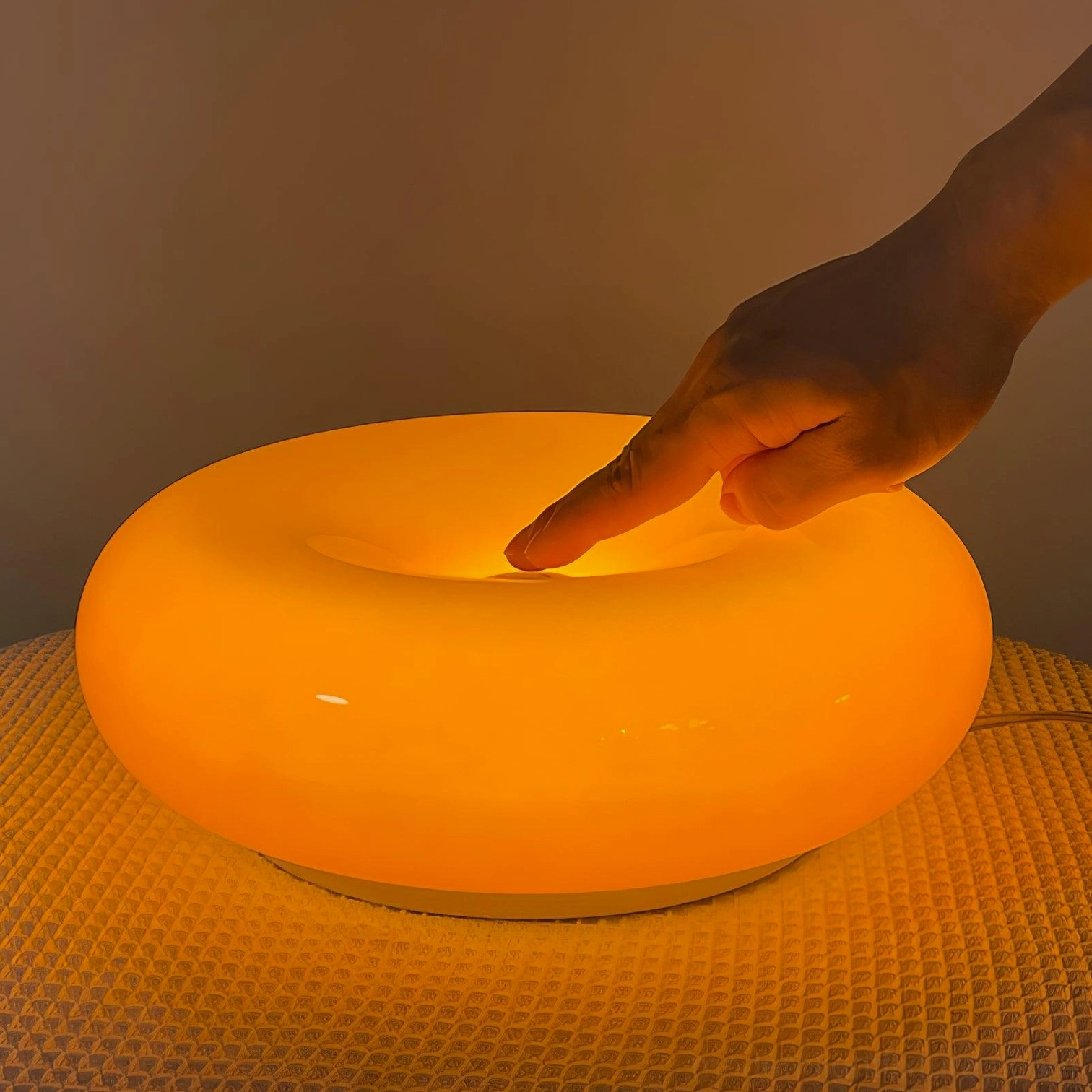 Illuminated warm orange donut table lamp glowing on textured bedding with three-color LED light activated