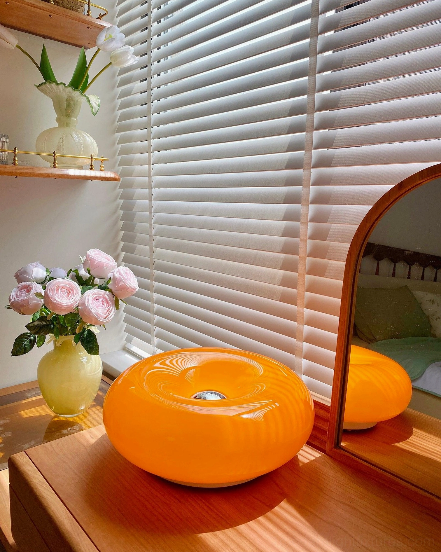 Orange donut lamp on wooden vanity with window blinds showing glossy finish and mirror reflection