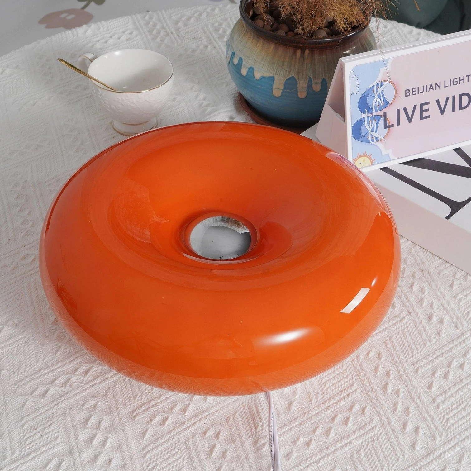 Orange donut shaped table lamp overhead view on decorated side table with power cord visible