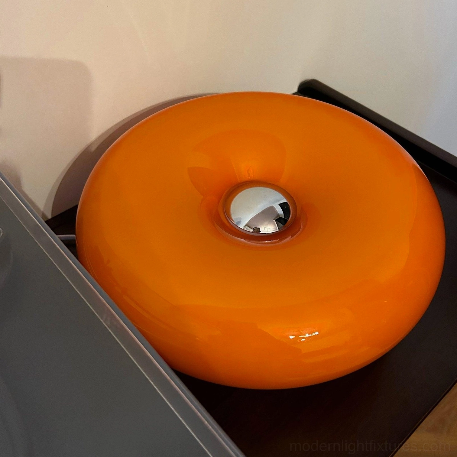 Donut table lamp side close-up view on dark wooden tray showing smooth glossy orange exterior