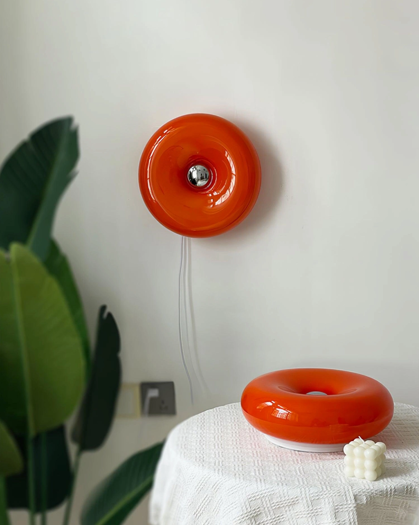 Donut wall lamp and matching donut table lamp in glossy orange, styled in home decor display setting