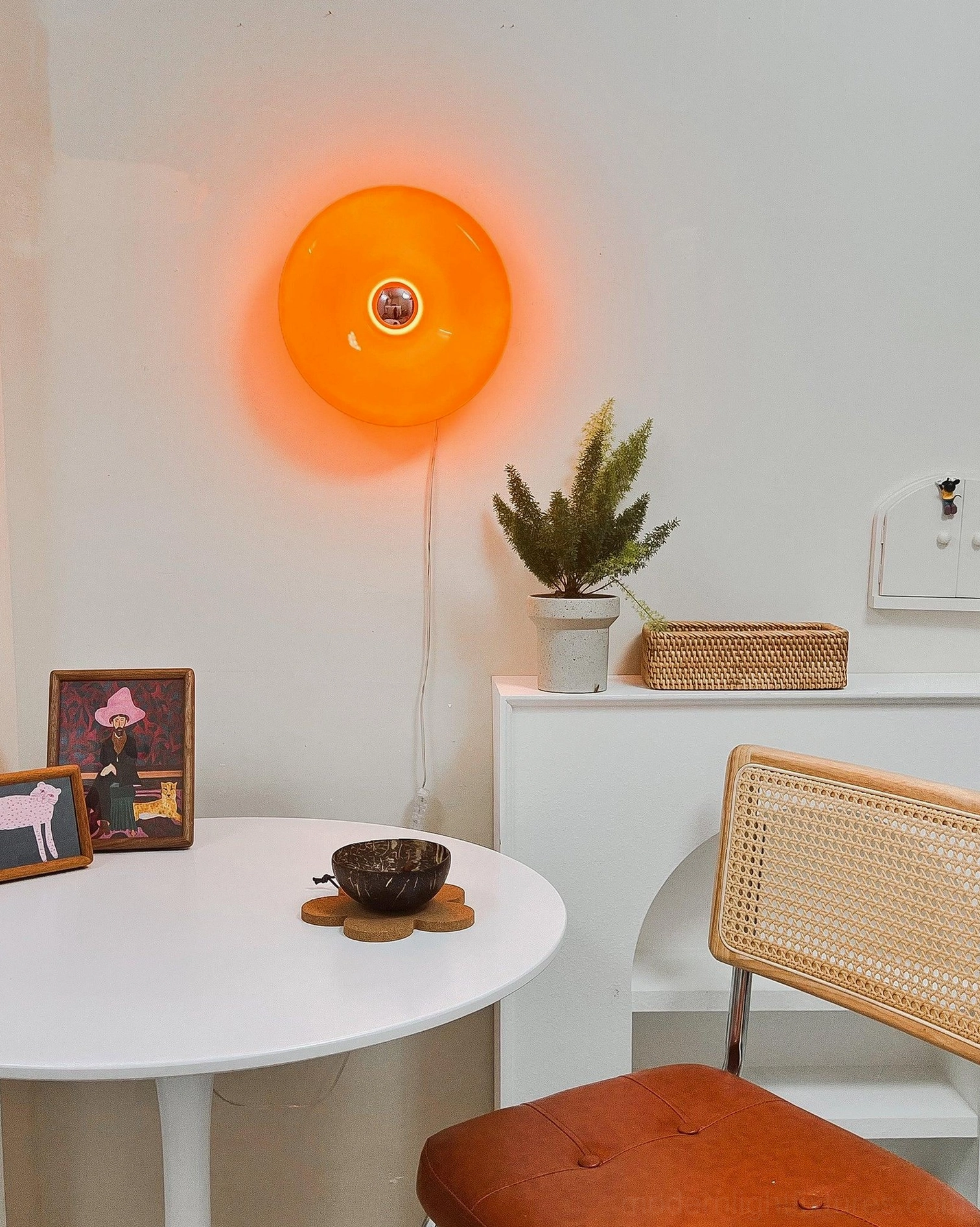 Orange donut wall sconce installed in modern dining corner with rattan furniture and warm retro styling