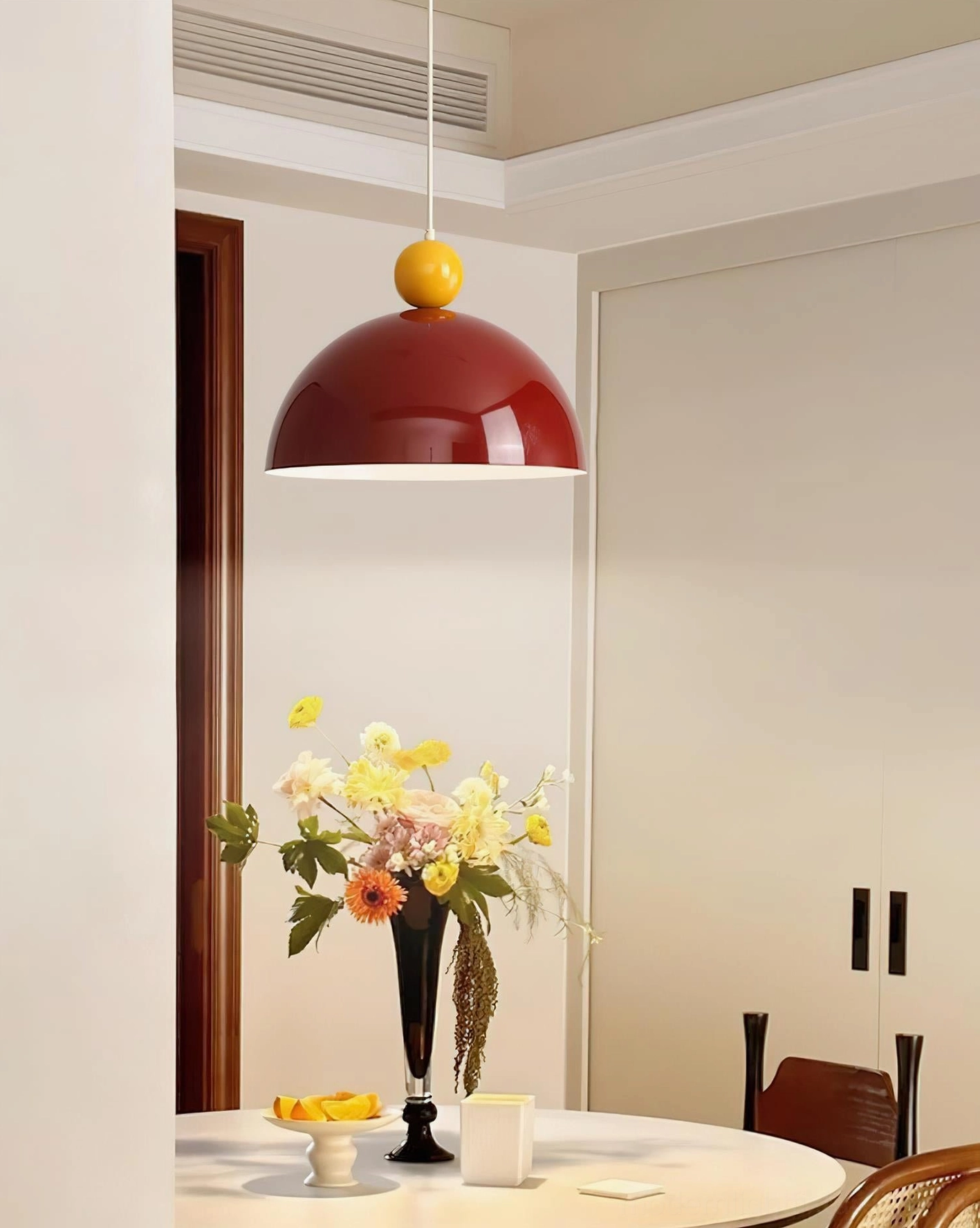 Dotto burgundy dome pendant lamp with yellow spherical accent, side view in modern minimalist dining space with floral table setting