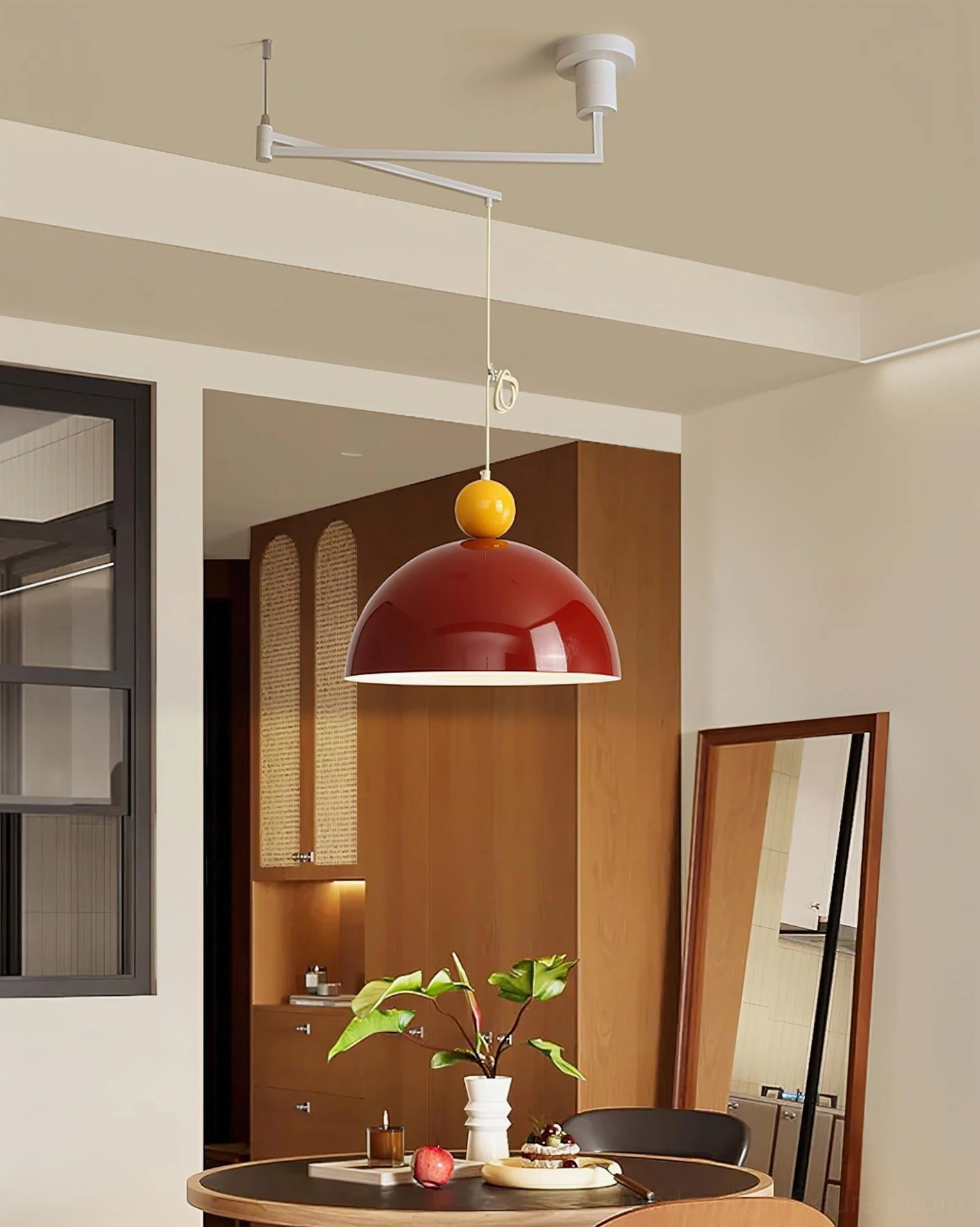 Contemporary swing arm pendant light with red shade hung over dining table in warm vintage home setting