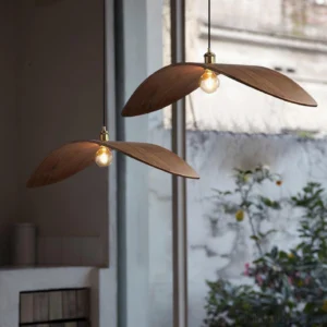 Two walnut wood leaf pendant lamps hanging at eye level in indoor-outdoor setting with warm brass accents and natural wabi-sabi aesthetic
