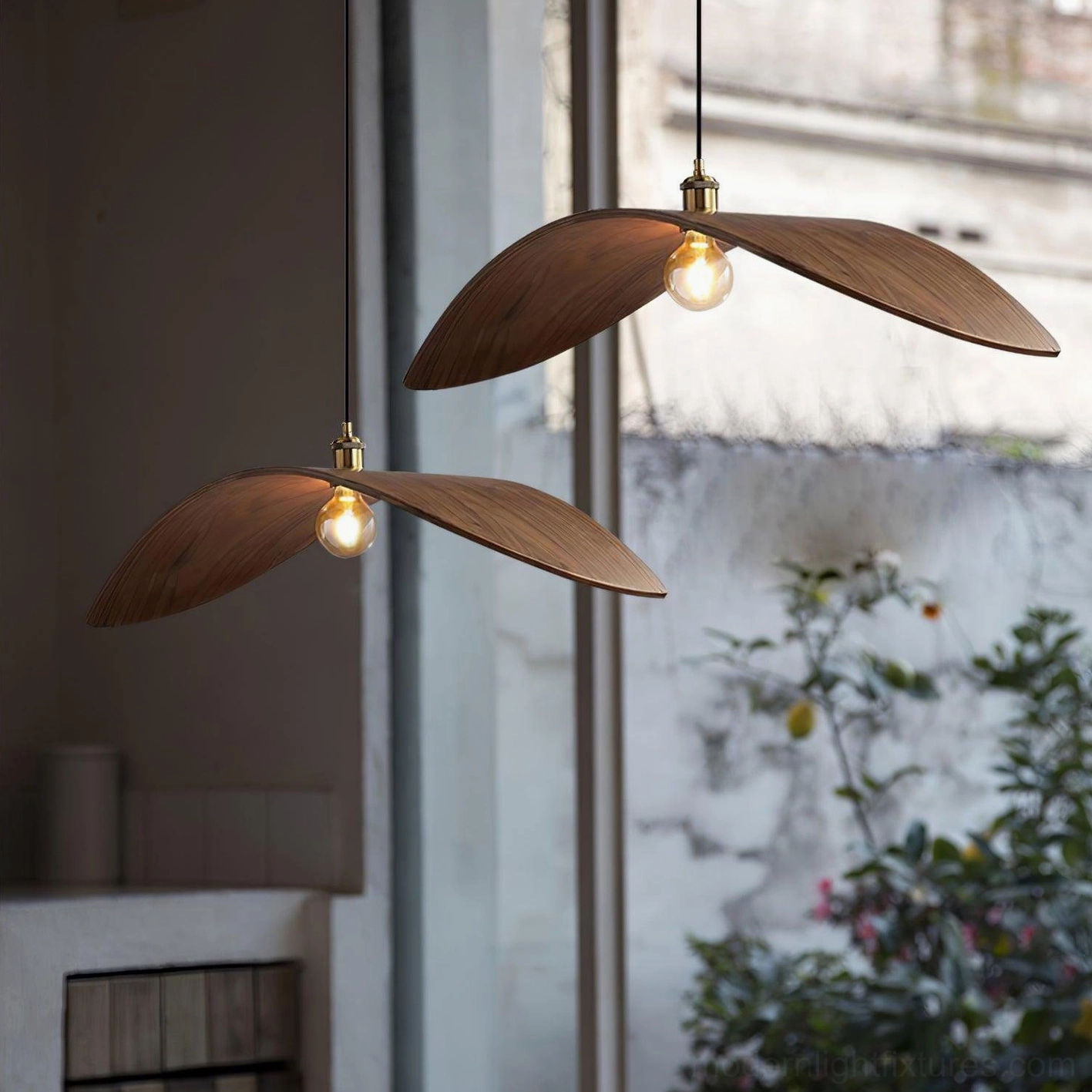 Two walnut wood leaf pendant lamps hanging at eye level in indoor-outdoor setting with warm brass accents and natural wabi-sabi aesthetic