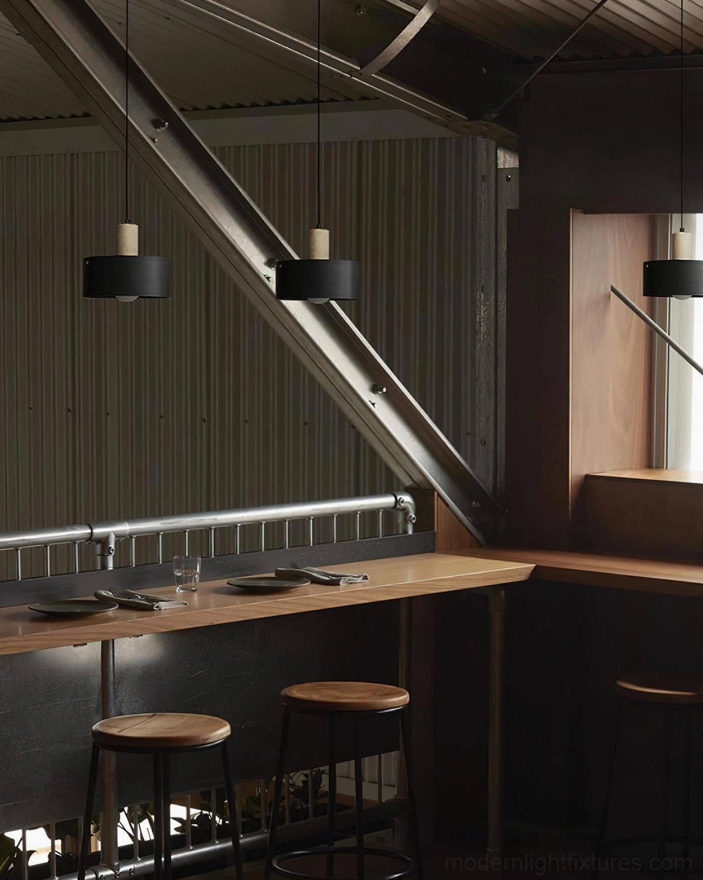 Multiple matte black Dovira drum pendant lights suspended in commercial cafe bar interior with exposed metal truss and industrial minimalist atmosphere