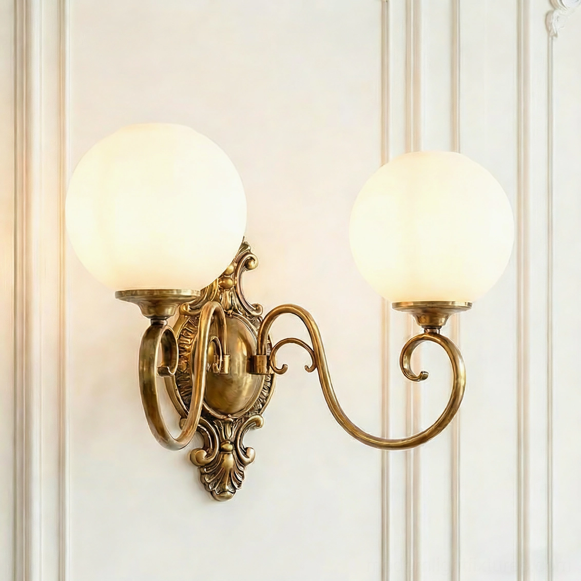 Dual-head ornate brass wall sconce with white glass globes, symmetrical baroque design