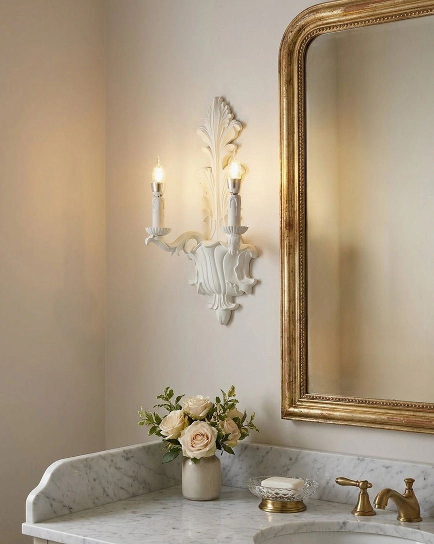 Dual-light carved wall sconce above bathroom vanity with gold-framed mirror and marble countertop
