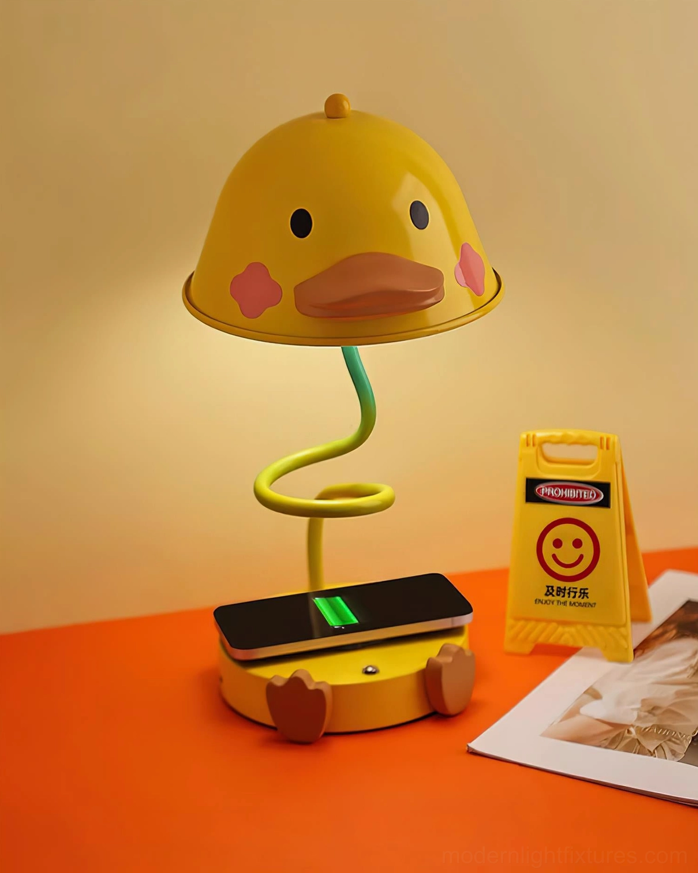 Whimsical duck desk lamp with warm ambient glow on orange display surface with charging phone