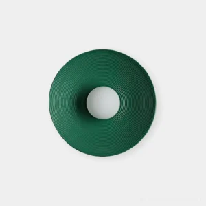 Echo Coil dark green ribbed circular wall sconce in minimalist wabi-sabi flat lay studio setting, top-down view showing concentric groove texture detail