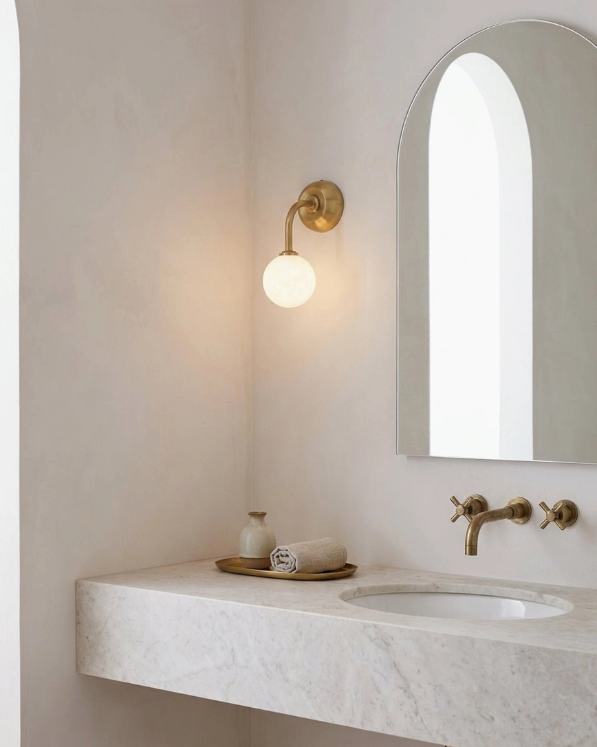 Bathroom vanity Elio wall sconce with arched mirror and marble countertop reflecting warm light