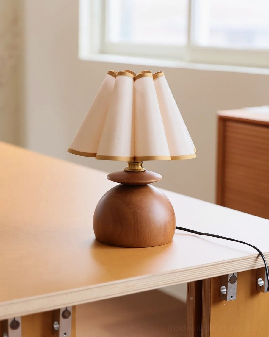 Elmora pleated fabric table lamp front view showing compact walnut base and geometric pleated shade design on light wood surface