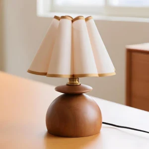Elmora table lamp low-angle oblique view showing smooth walnut texture and geometric pleated fabric shade with gold trim