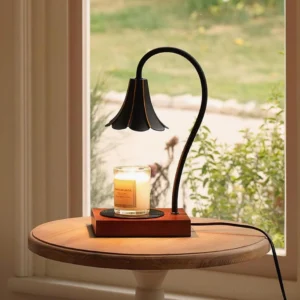 Modern botanical candle warmer table lamp styled by residential window with lit scented candle and garden view backdrop