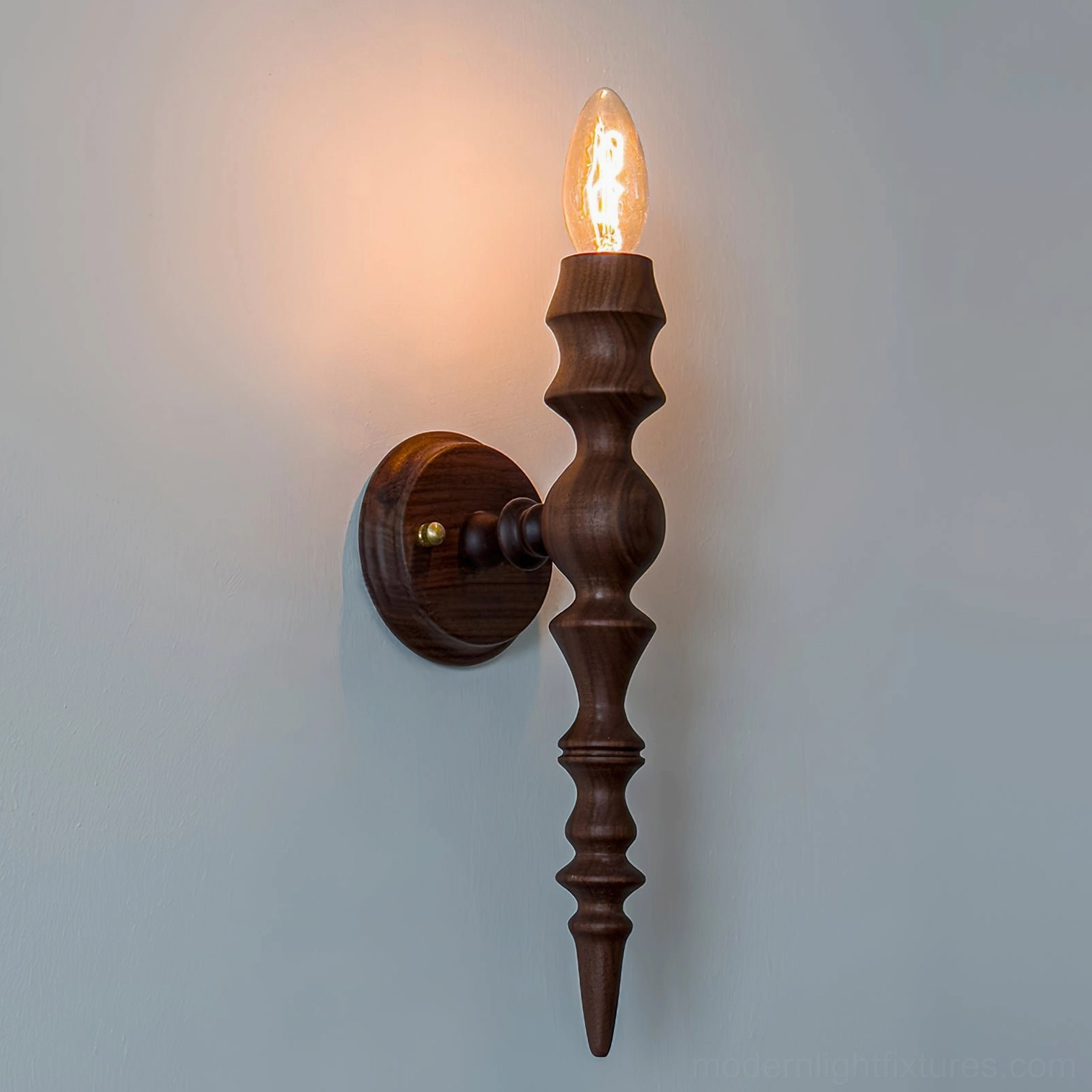 Eloise walnut wall sconce mounted on residential wall displaying warm candlelight glow