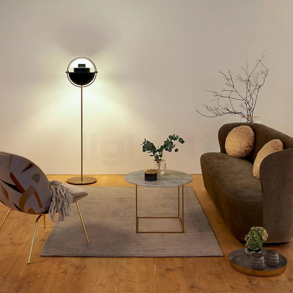 Semi-enclosed spherical Elvira floor lamp with brass pole and black shade beside sofa in warm wood-floored living room