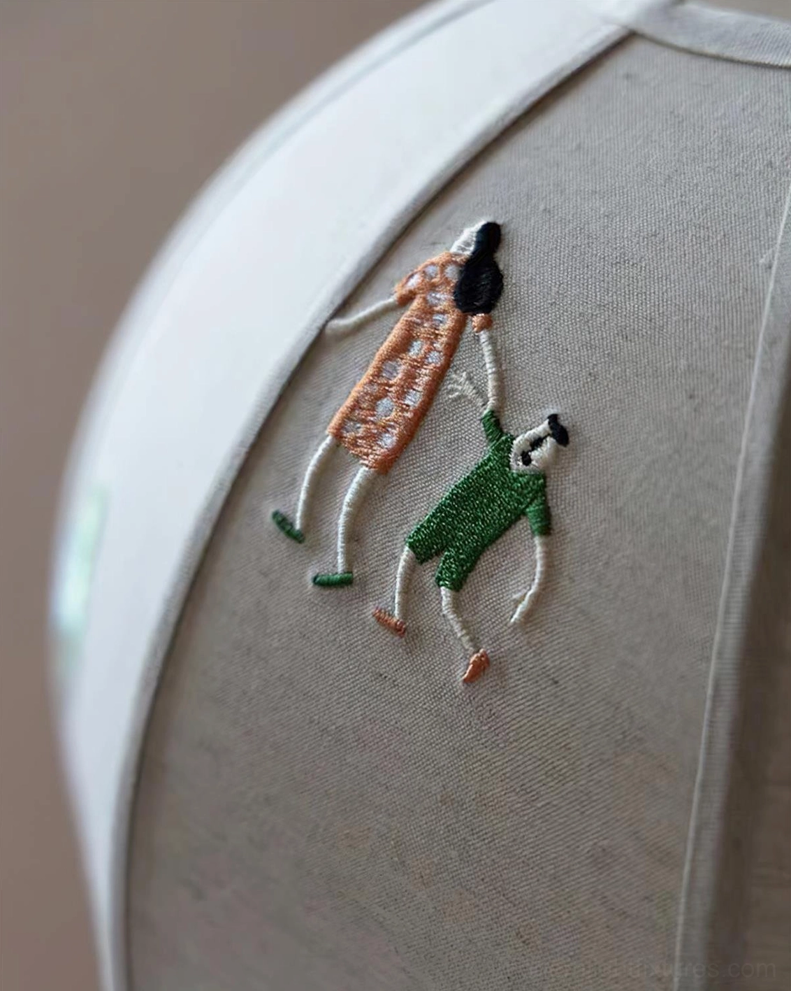 Close-up macro view of embroidered linen fabric shade showing detailed stitching of cartoon human figures and woven texture