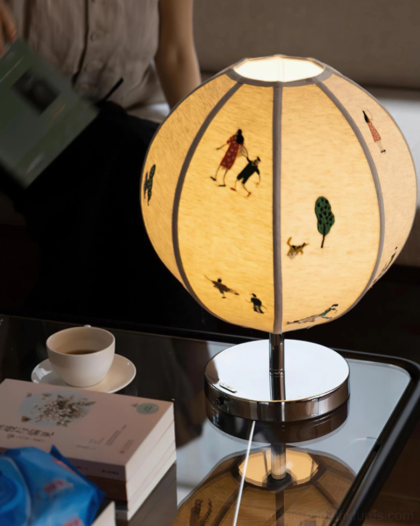 Embroidered narrative table lamp displaying full spherical shade with chrome metal base and integrated LED warm white lighting