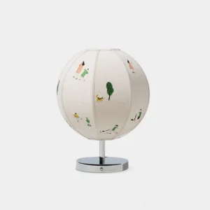 Embroidered narrative table lamp with spherical white fabric shade featuring cartoon human and plant motifs, polished chrome round base, studio front view
