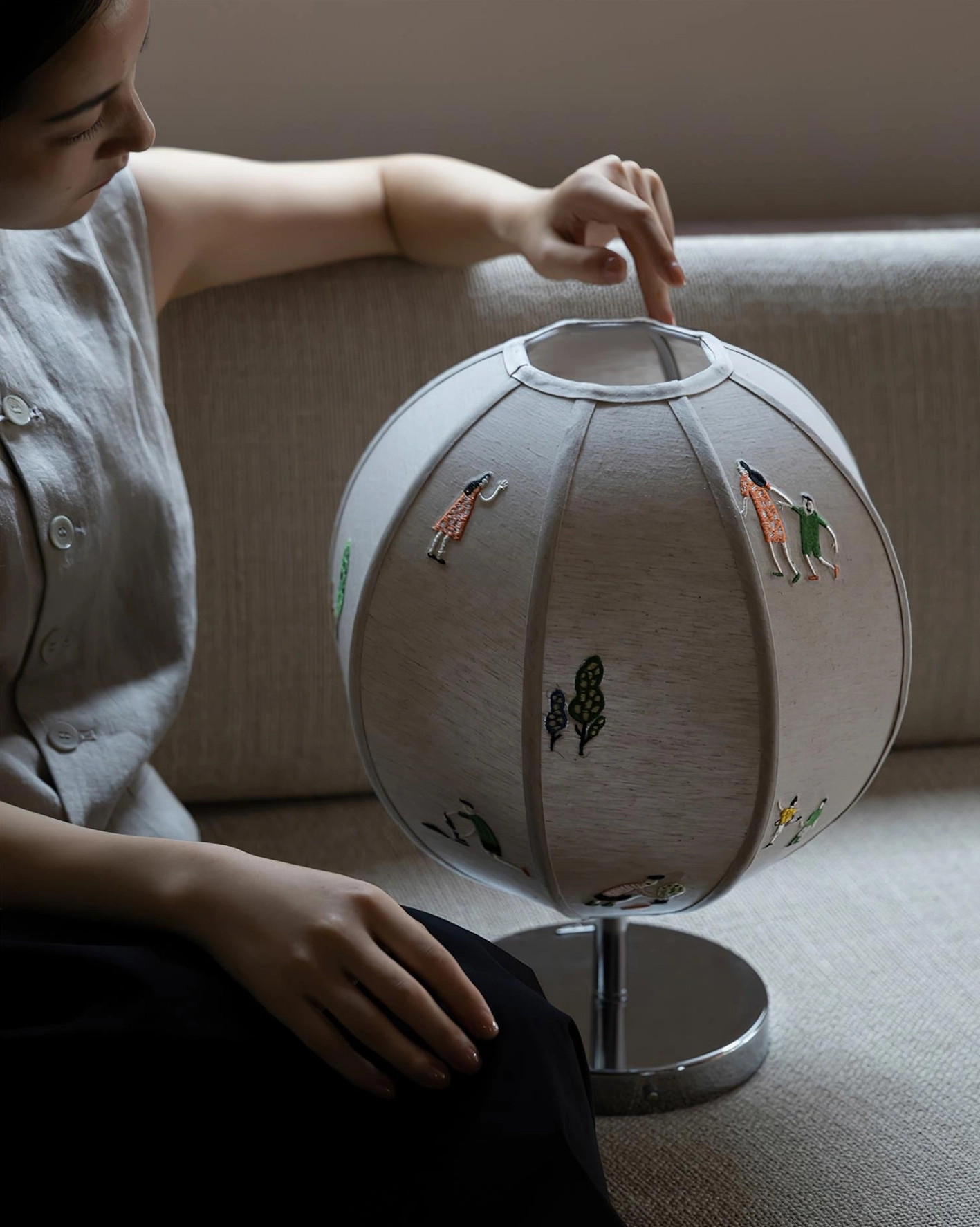 Detached fabric shade of embroidered table lamp on chrome metal stand in living room with sofa, showing separation of components
