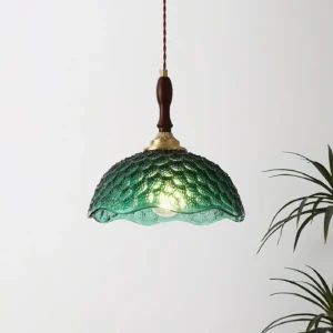 Green glass pendant light hanging indoors with twisted textile cord, vintage mid-century design with houseplant