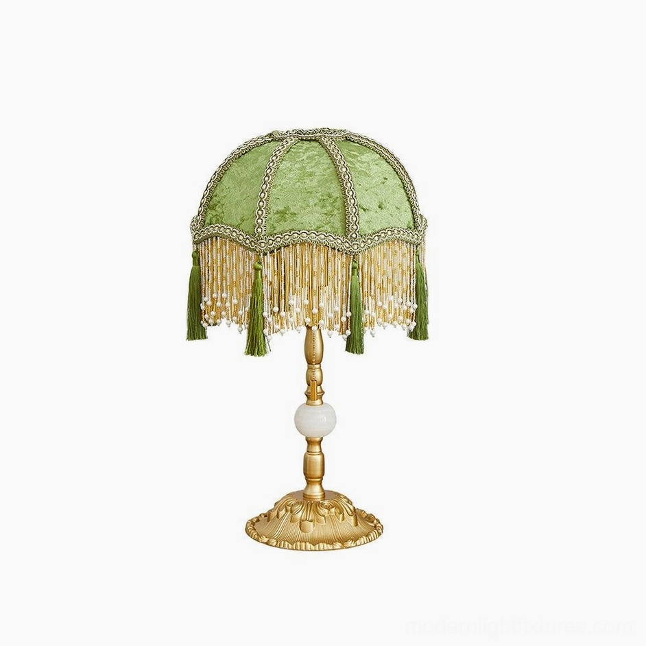 Unlit emerald green velvet table lamp with gold base and white spherical accent on white background
