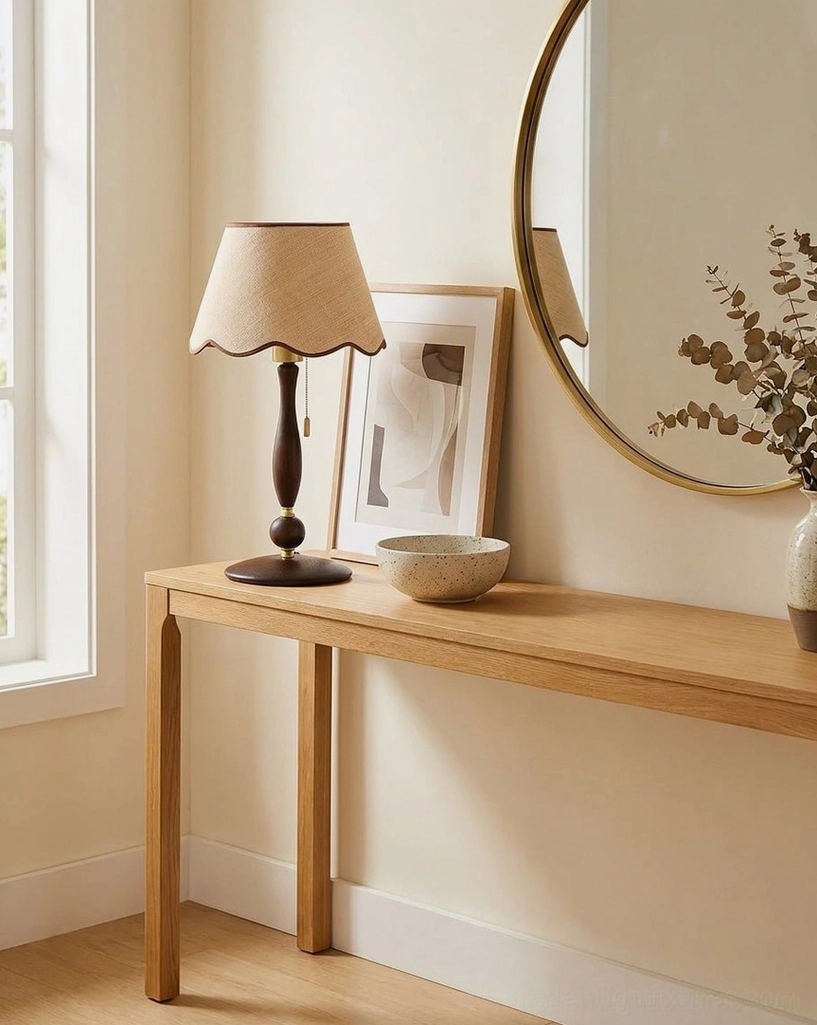 Scalloped linen table lamp on long entryway console table with round mirror and framed wall artwork - side angle view