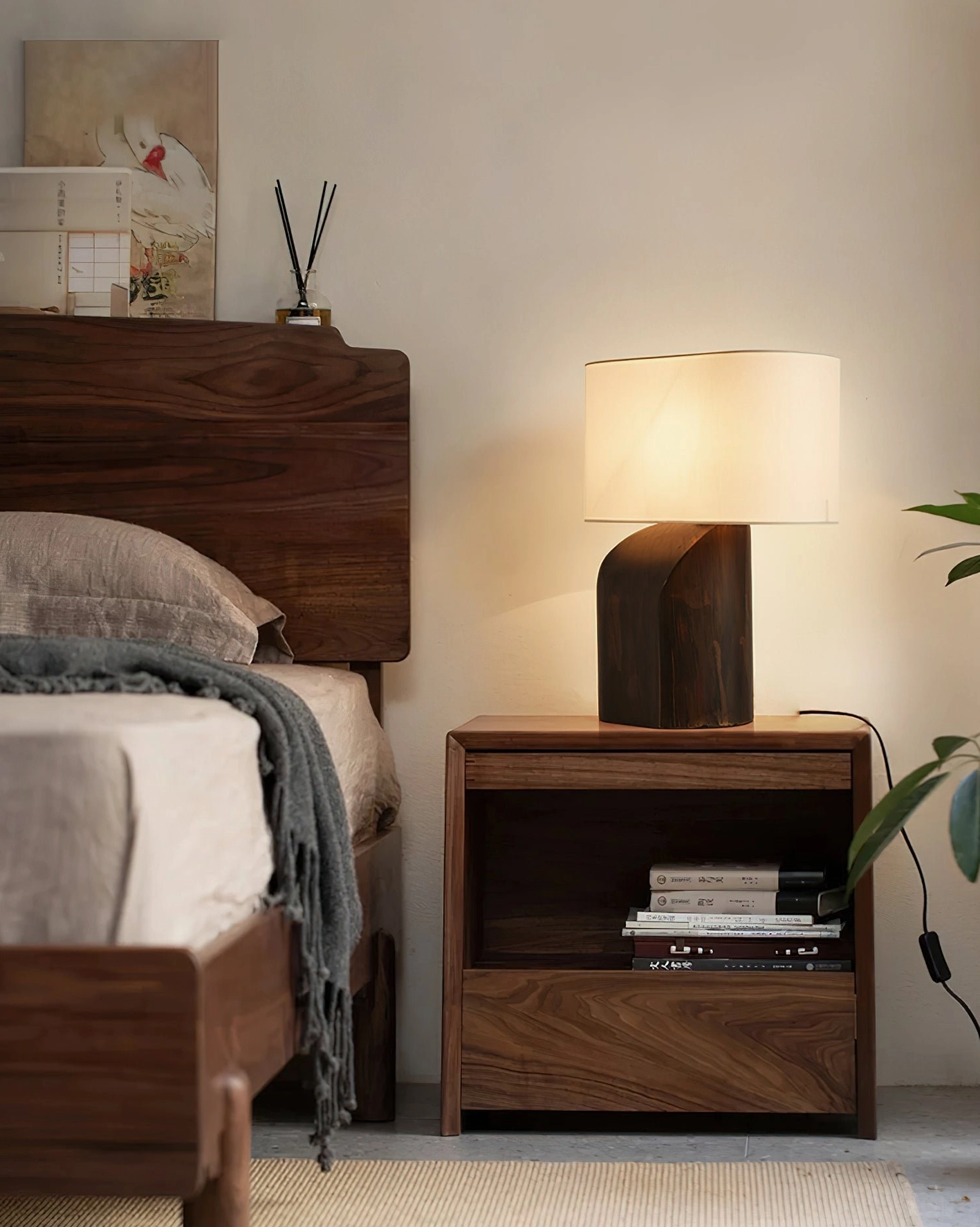 Dark wood sculptural table lamp on bedroom side table, side angle view with open storage and warm lighting