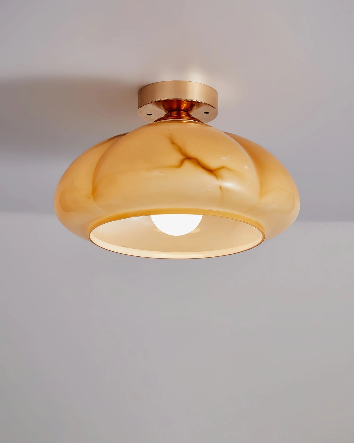 Modern semi-flush ceiling light with marbled amber glass shade and brass hardware, three-quarter front view