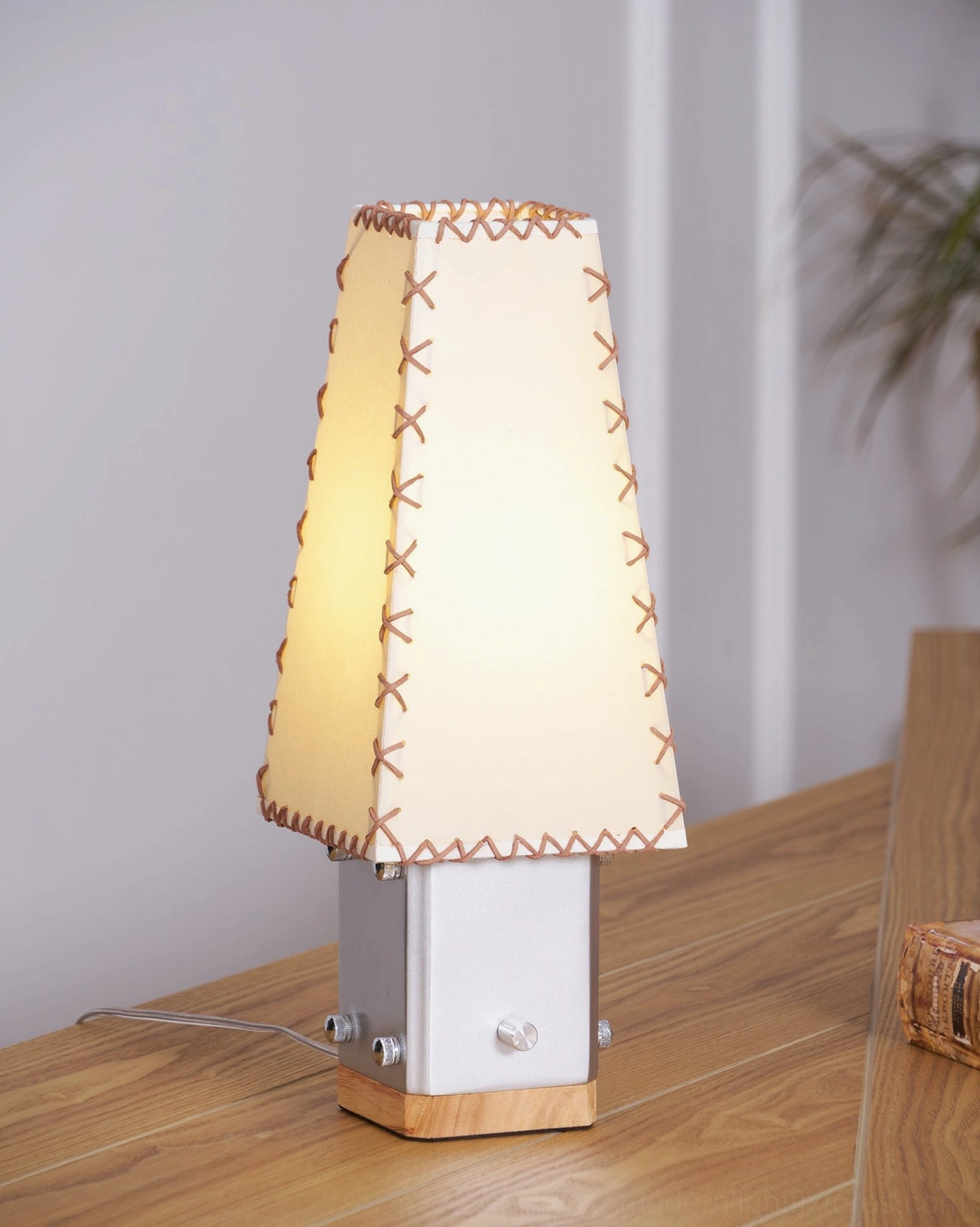 Estela table lamp creating warm ambient light in bedroom setting with plant backdrop