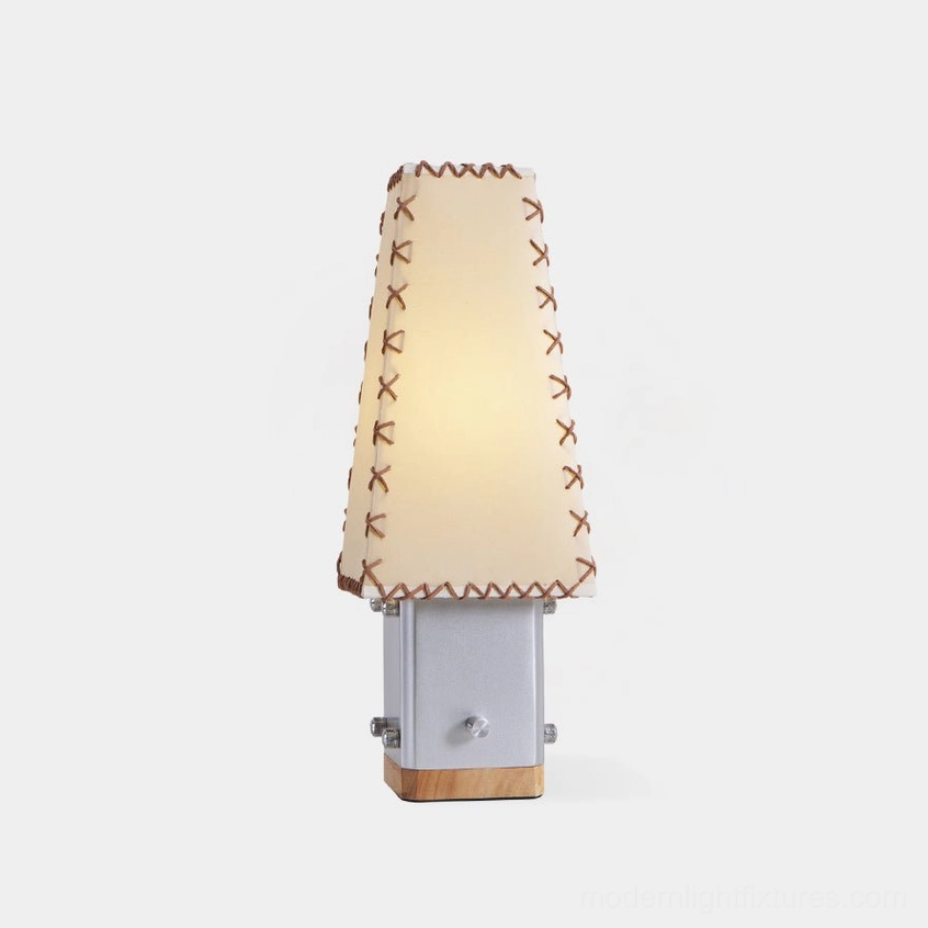 Estela handcrafted table lamp front view showing tapered fabric shade with contrast stitching and geometric metal base with wood accents
