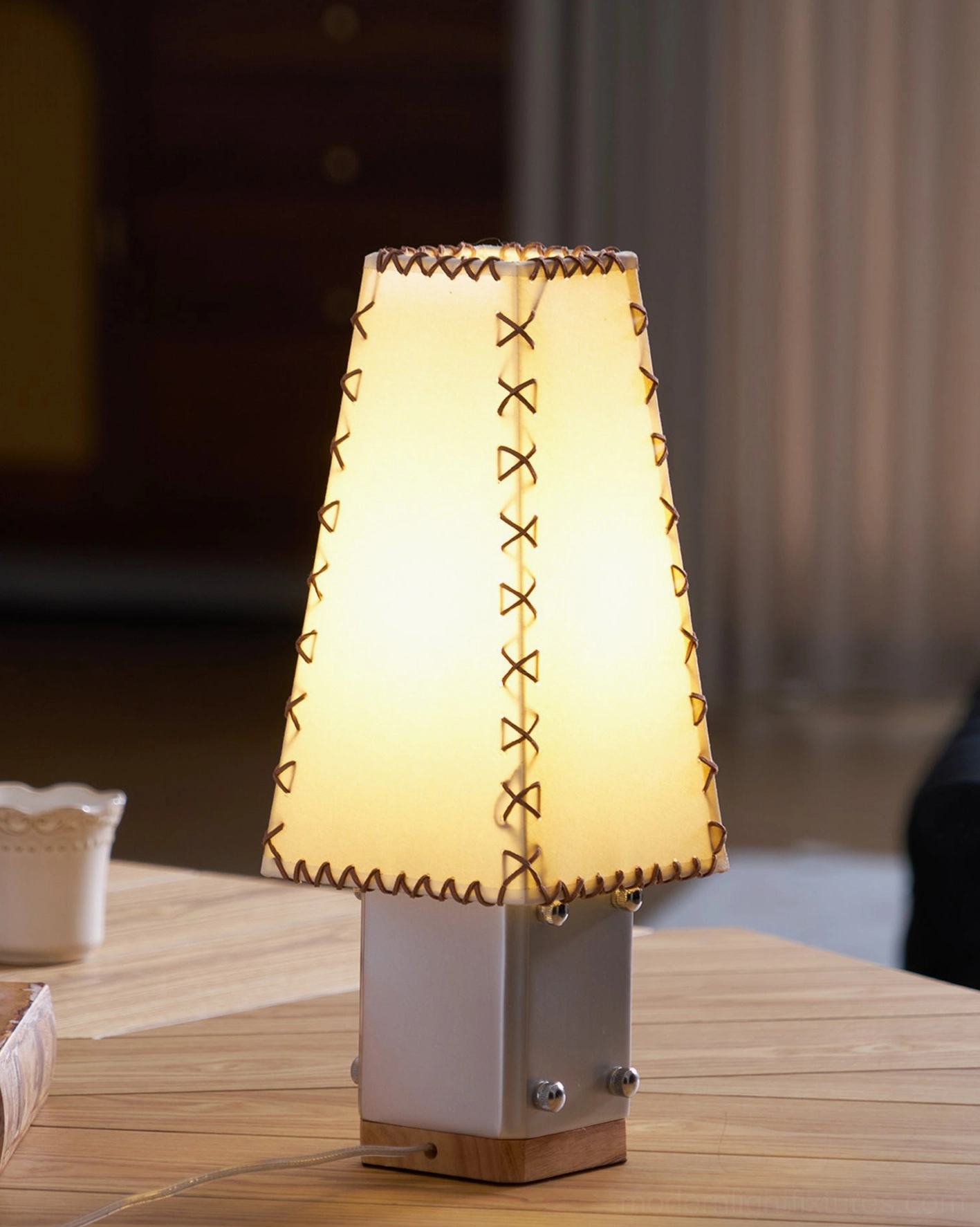 Estela handcrafted table lamp glowing on wooden table showcasing metal base and parchment shade