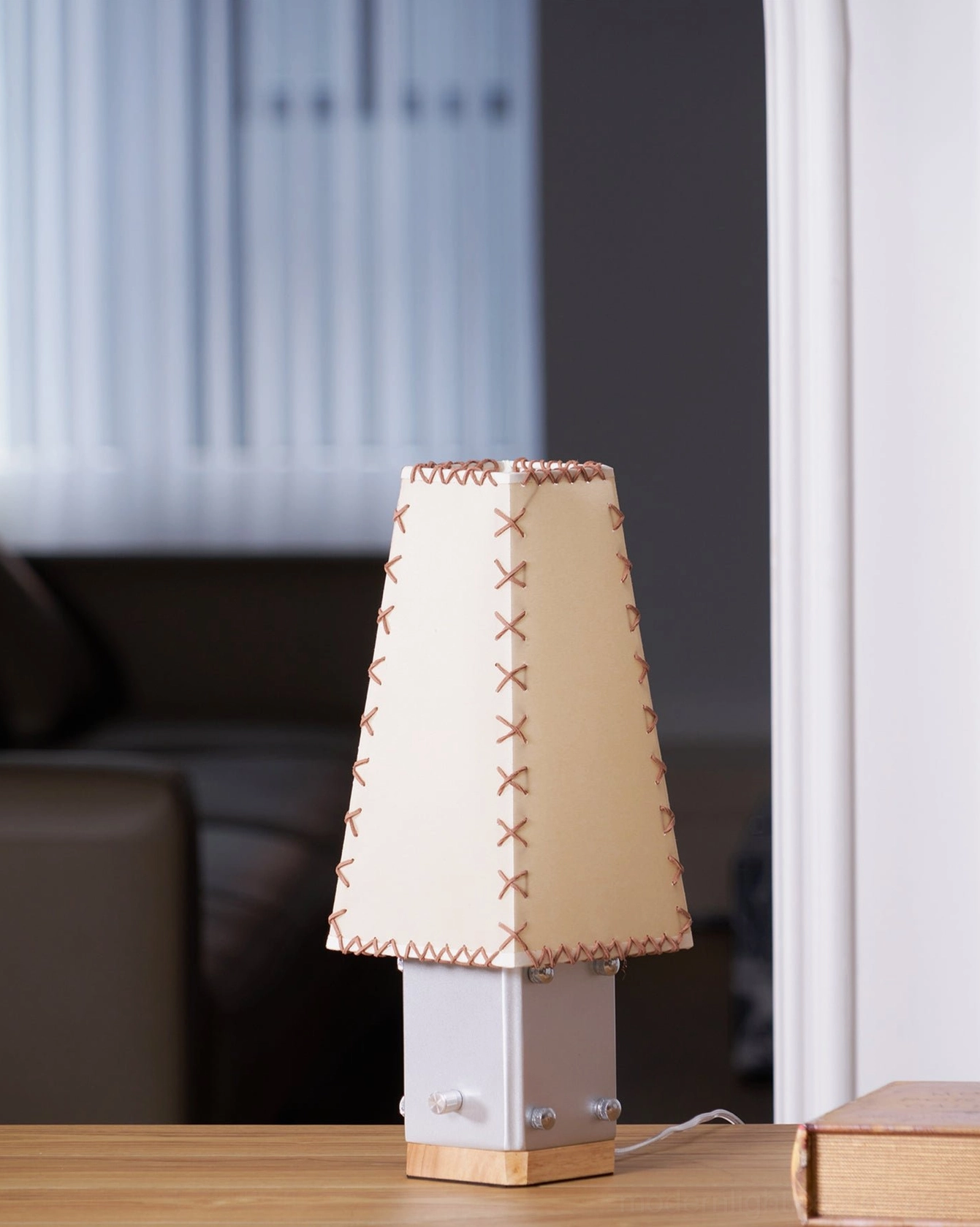 Estela table lamp on living room side table with sofa and window blinds in background