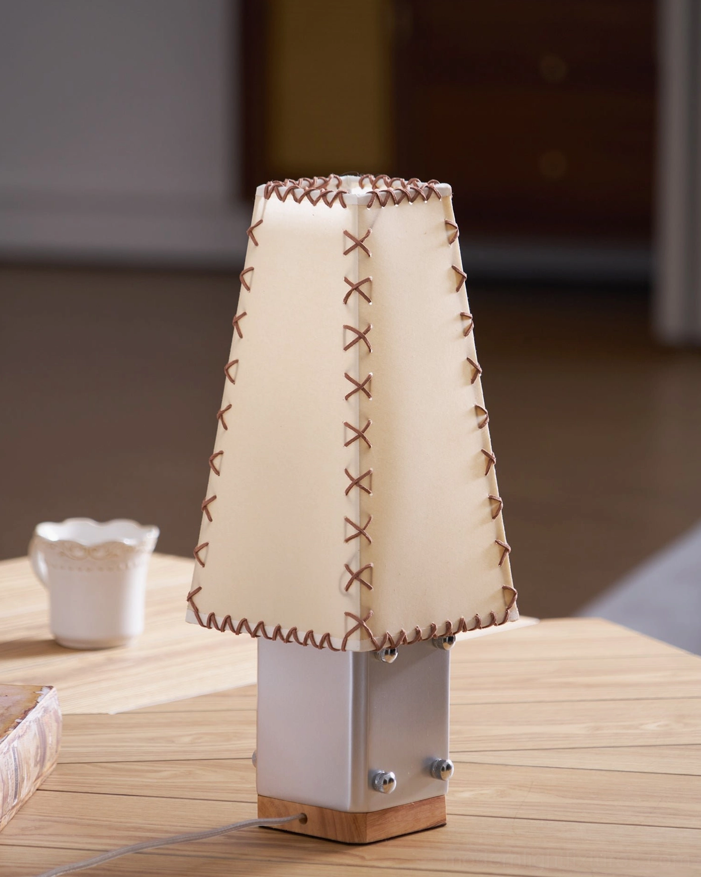 Estela table lamp unlit showing trapezoidal tapered shade detail on wooden surface with ceramic cup