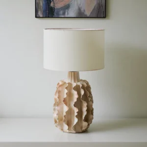 Modern ceramic table lamp with hand-glazed warm sand finish and fabric drum shade on shelf