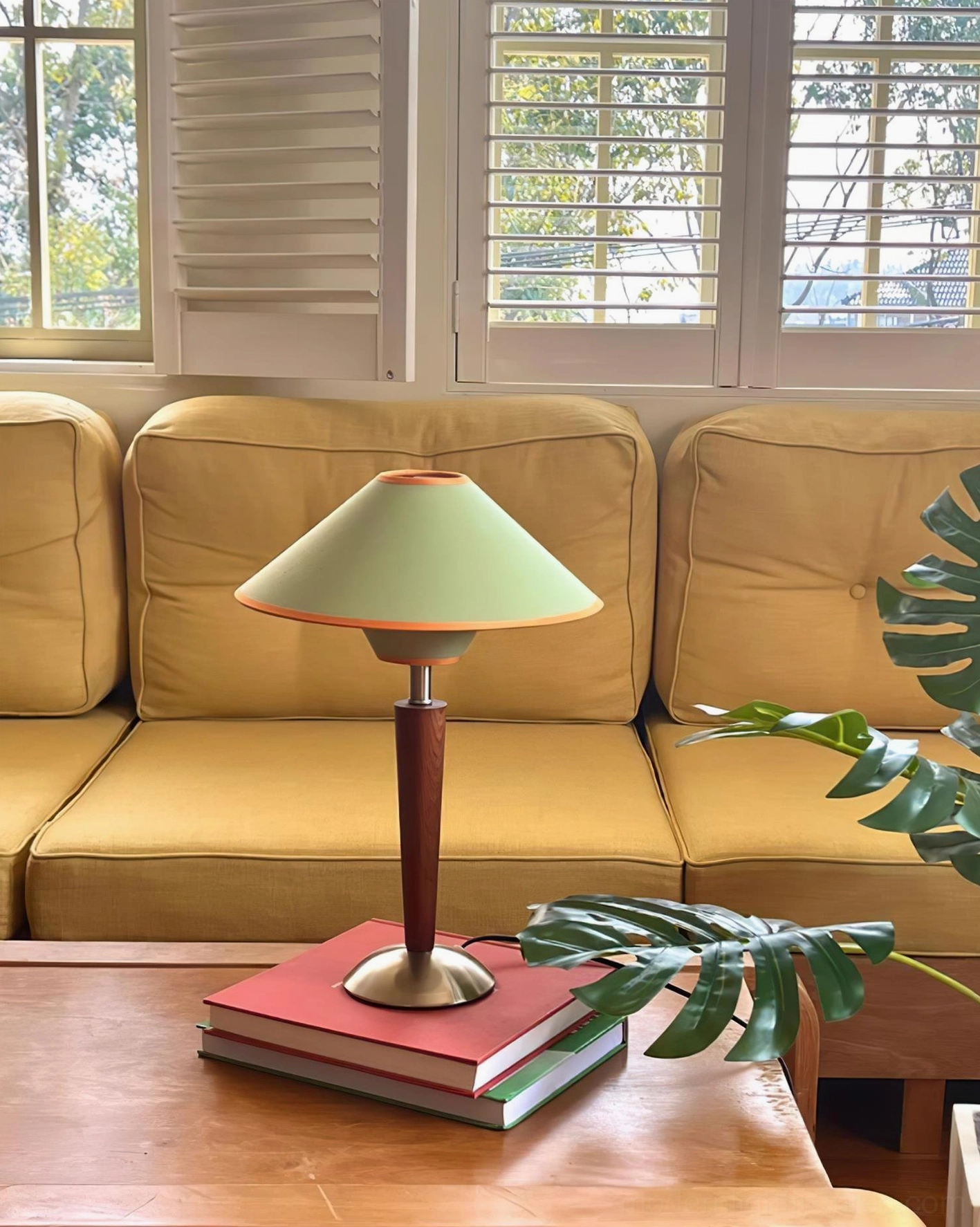 Contemporary fabric shade table lamp in living room with yellow sofa, stacked books, and green foliage decor