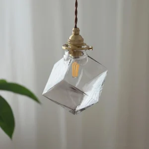 Felix clear glass cube pendant light in brass gold, side hanging view with natural indoor lighting and sheer curtain backdrop