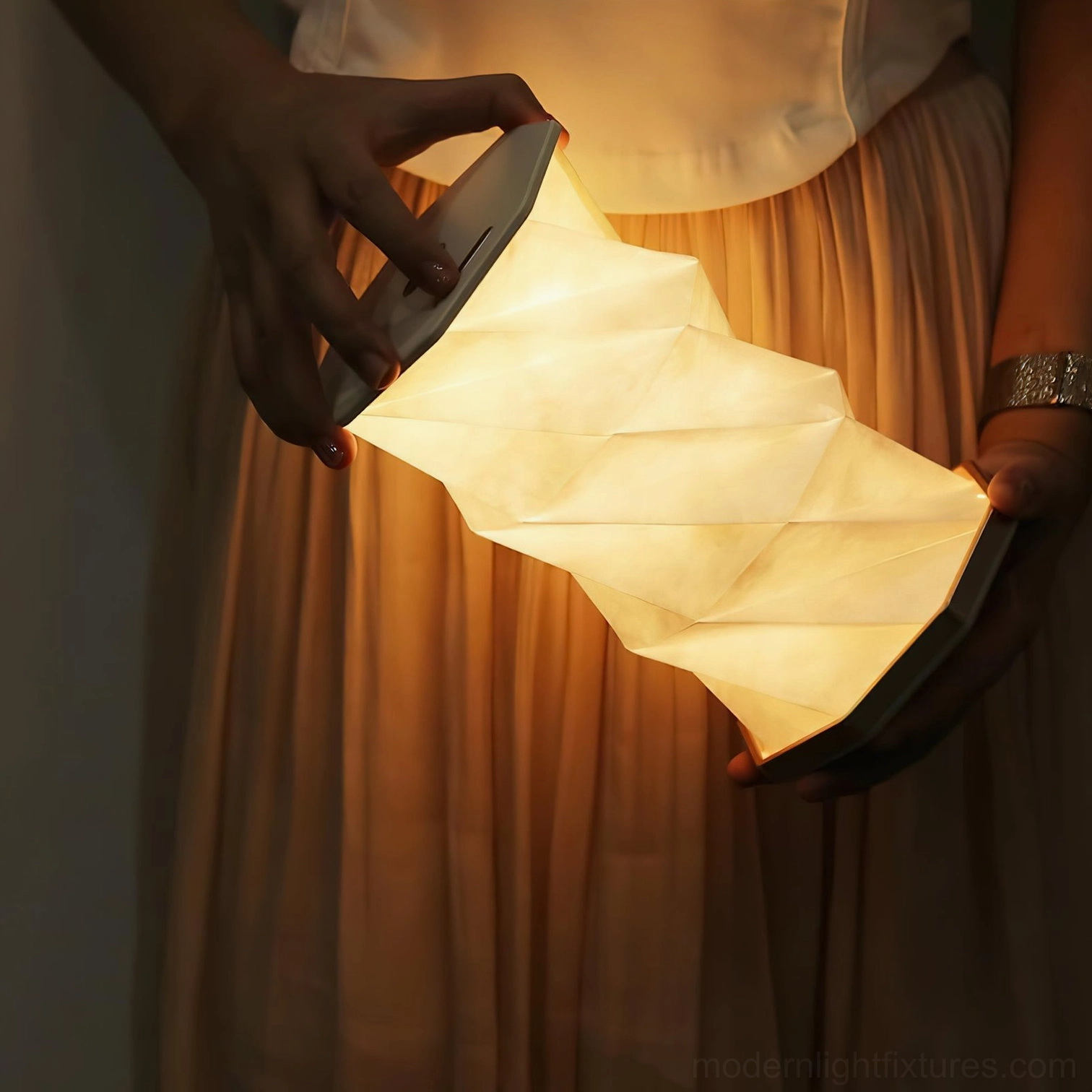Fida Fold Paper Table Lamp in hand showing flexible twisted shade design with illuminated warm light and touch control panel on top