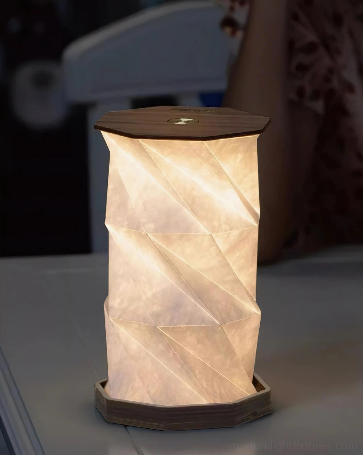 Glowing Fida Fold Paper Table Lamp with warm illuminated twisted shade and dark brown wooden base positioned on living room side table