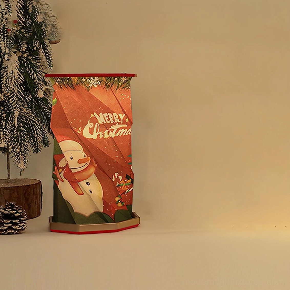 Fida Fold Paper Christmas Table Lamp with festive snowman print cylindrical origami shape displayed on shelf with holiday decor