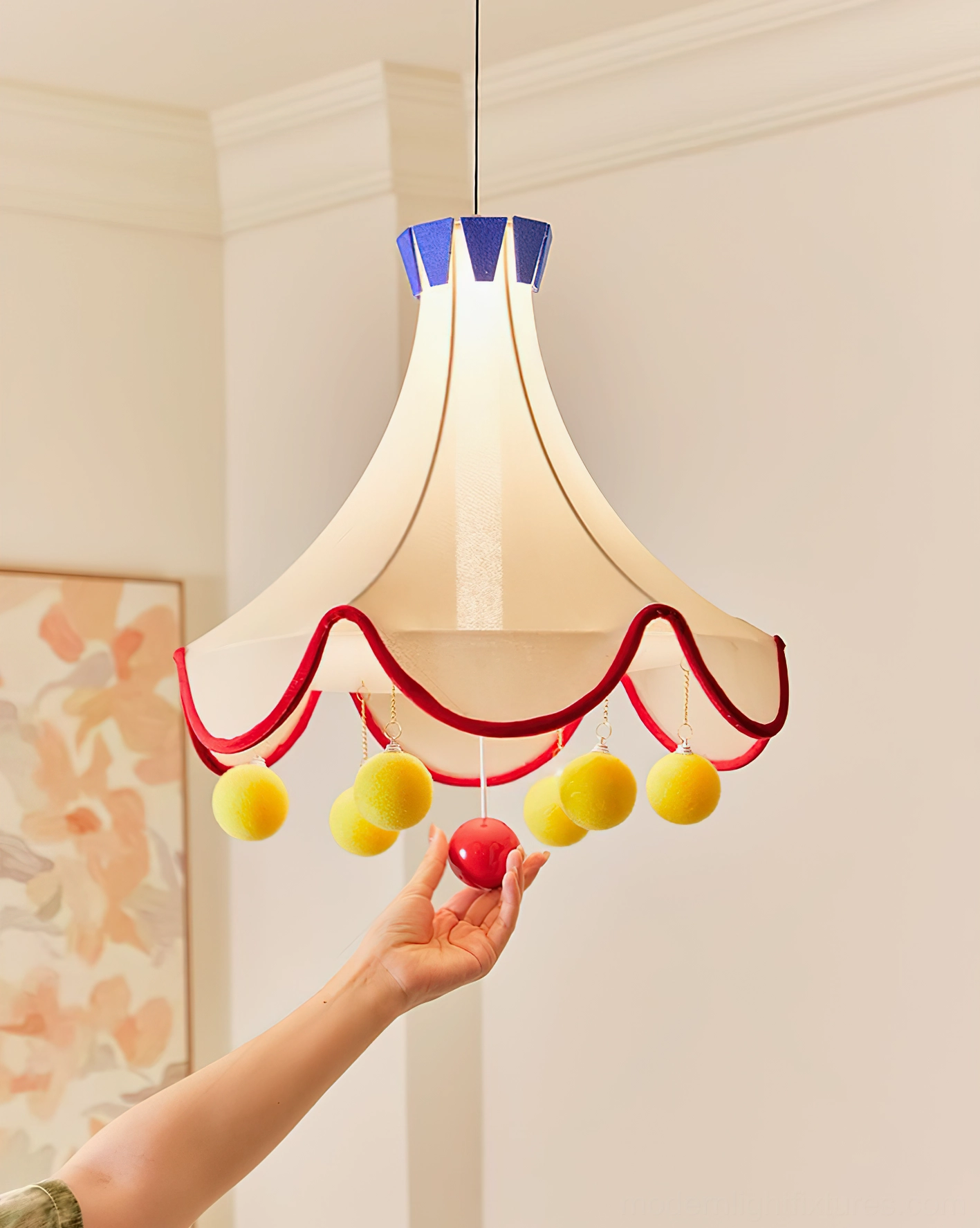 Finaflor circus tent pendant light three-quarter front view in residential hallway with wall art and hand interaction with red hanging pom-pom decoration