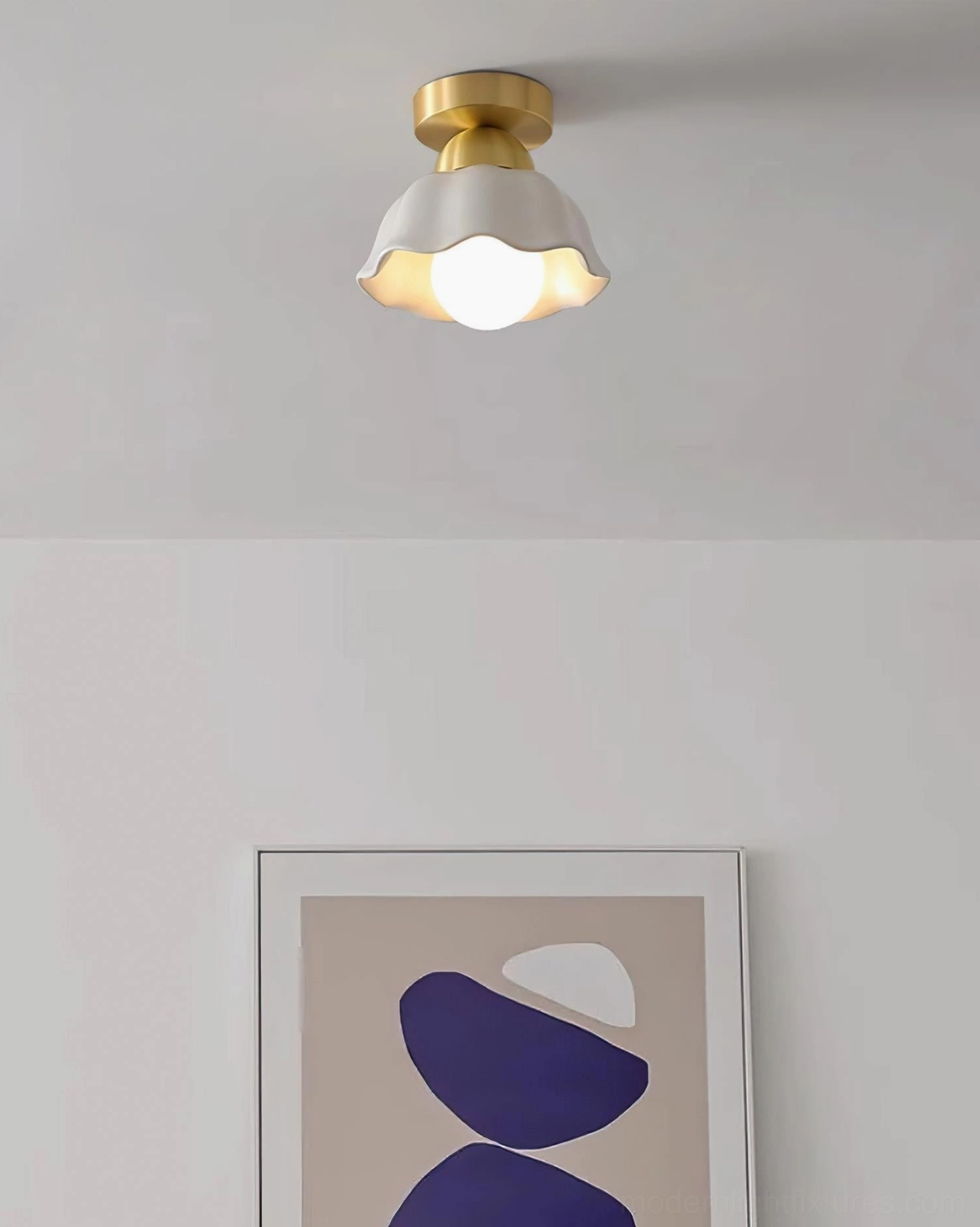 Finley flower-inspired ceiling light illuminated above framed artwork, warm brass and ceramic fixture creating ambient glow in bedroom or hallway