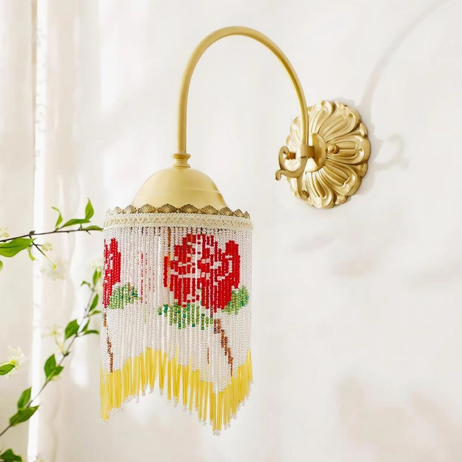 Vintage wall sconce with white beaded fringe and polished brass hardware photographed in three-quarter view with decorative greenery
