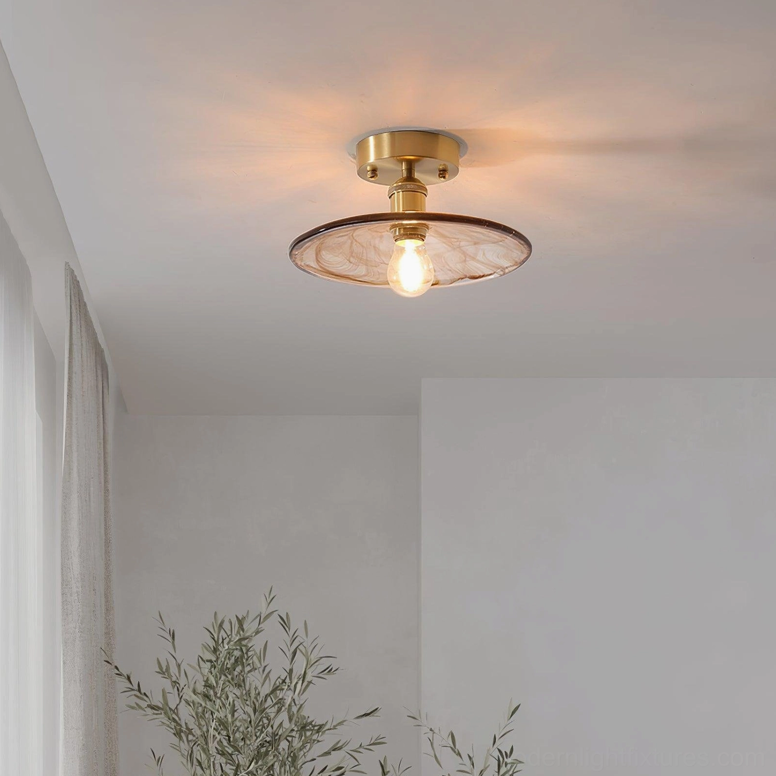 Flat disc amber glass semi-flush ceiling light with brass base installed in minimalist corridor interior