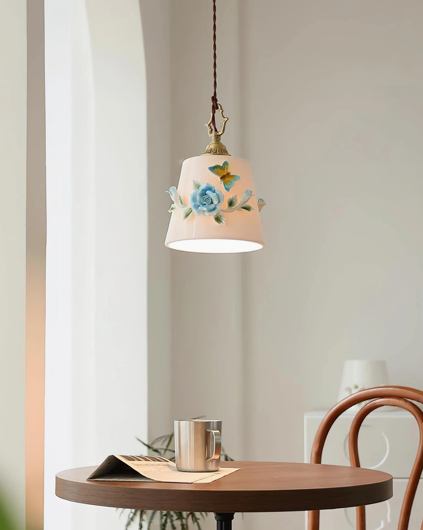 Handpainted floral ceramic pendant light above minimalist wooden dining round table with warm daylight, vintage brass hardware botanical pendant