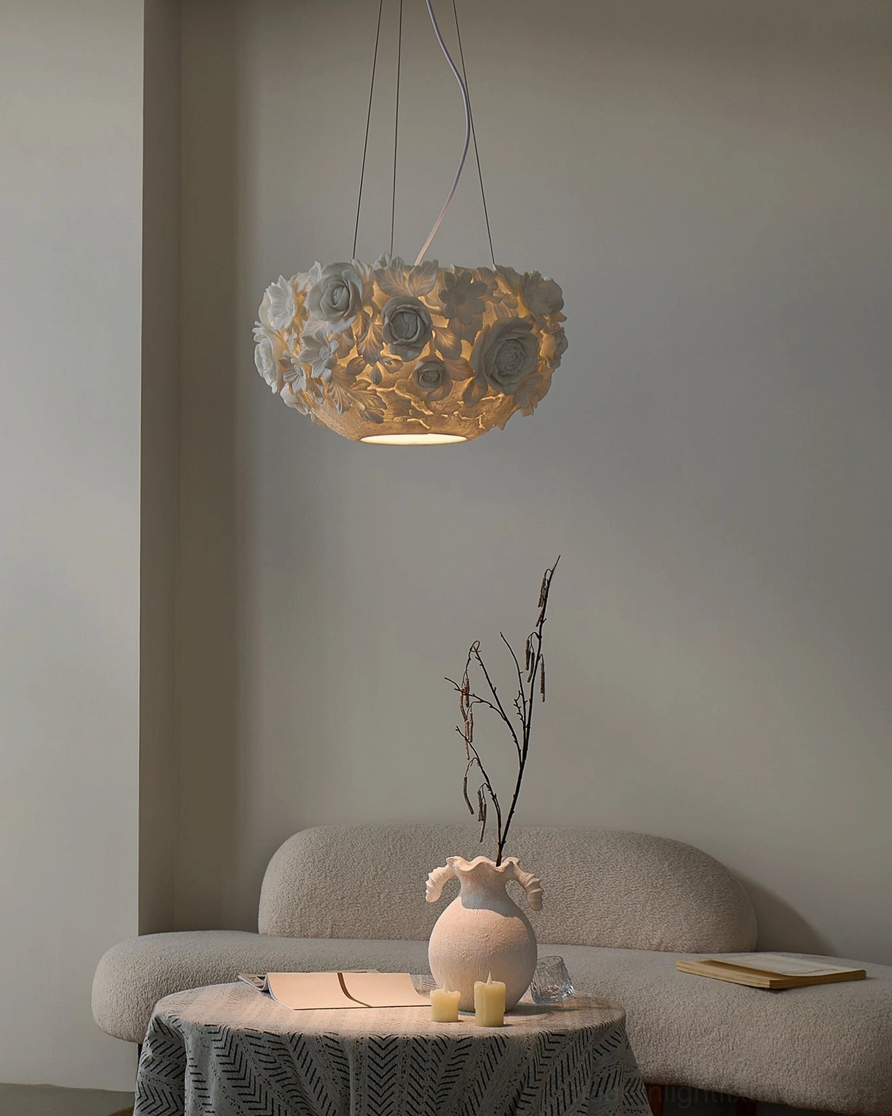 Ceramic floral pendant light glowing warmly above living room sofa and side table, showing sculptural shade design in home setting