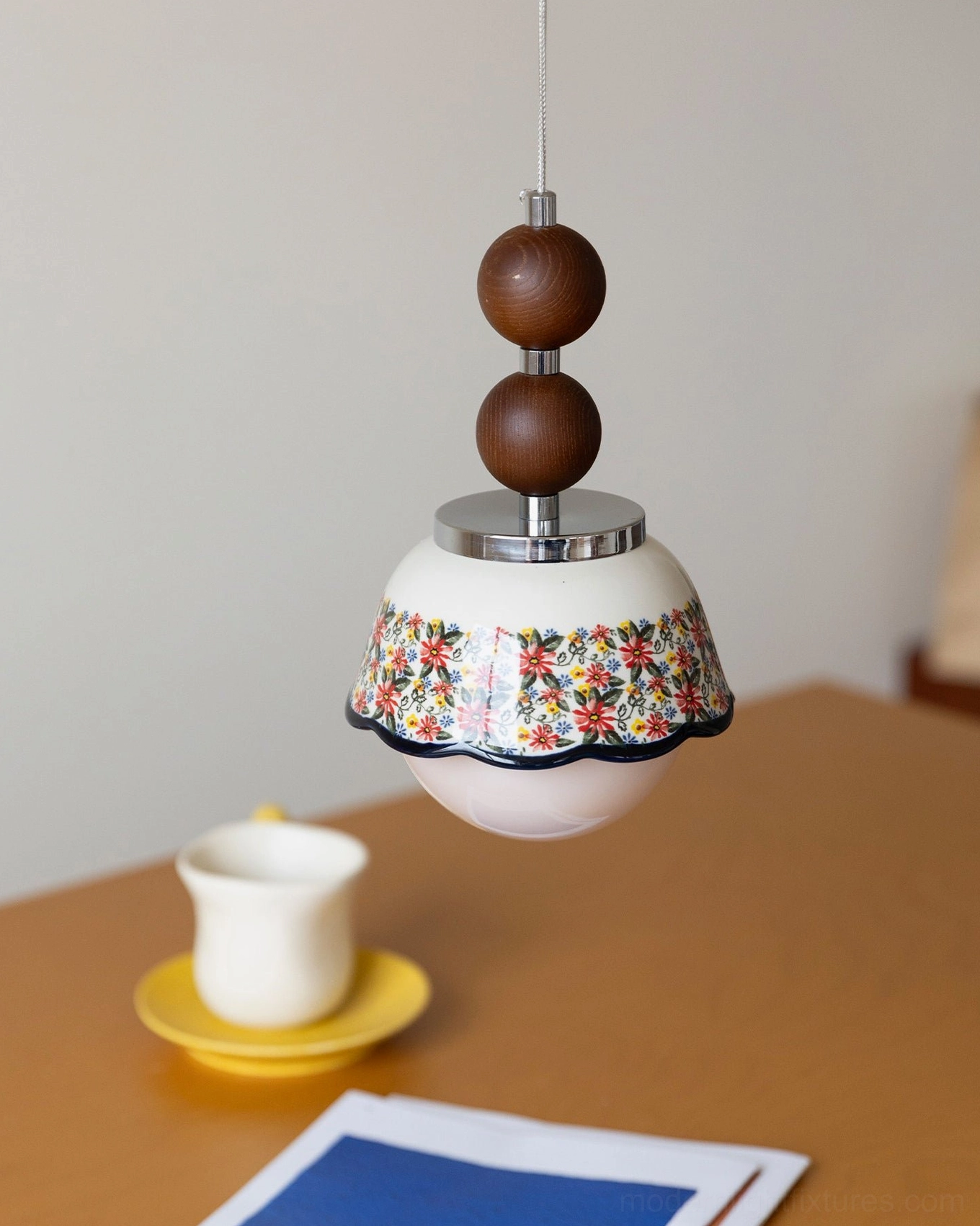 Floral pendant lamp hanging close-up over indoor tabletop with tea cup and stationery, cozy home tea corner intimate lighting
